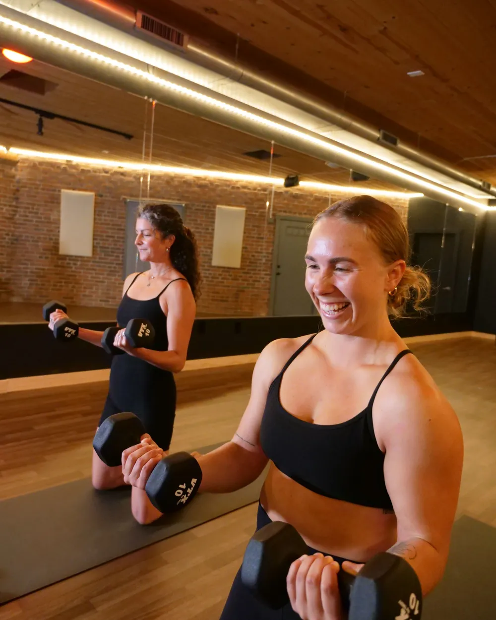 Alex Gaon smiling as she lifts hand weights in a bootcamp class